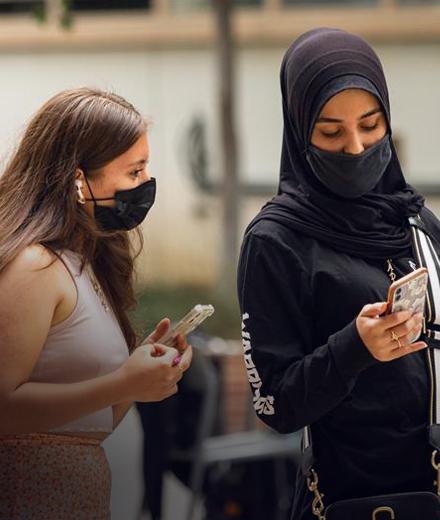 Two students with masks on, check their phones