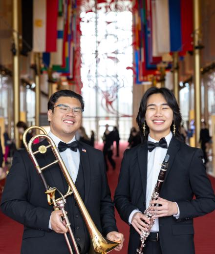 A trombone player and clarinet player stand in the Kennedy Center lobby smiling at the camera