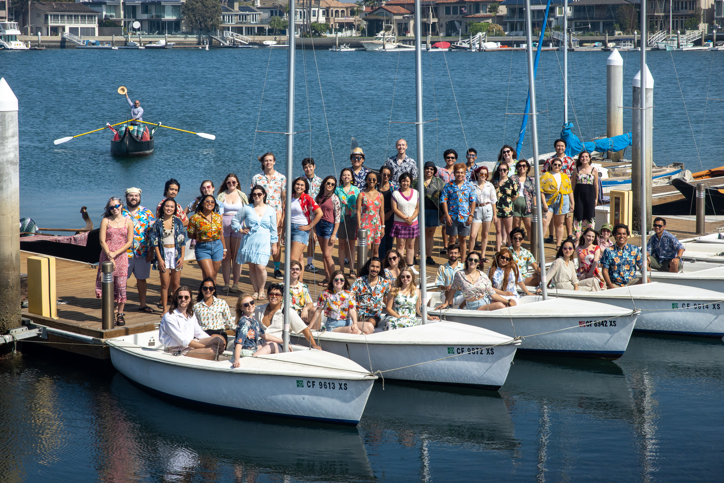 University Choir members standing on a dock in and around small boats.