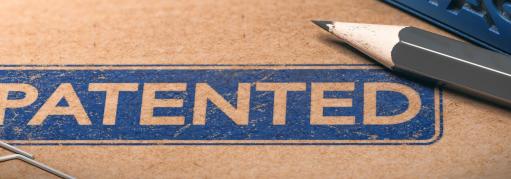 The word “Patented” is stamped in blue ink on a brown folder. The ink is surrounded by a paper clip and gray pencil.