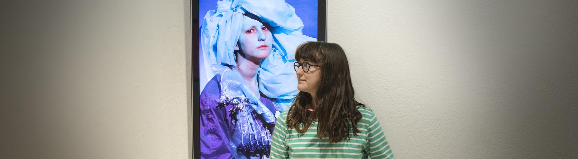 Sculpture student Juliet Johnson poses in front of her digital art project featuring herself titled “PINKEYE.” Photo by Joseph Philipson.