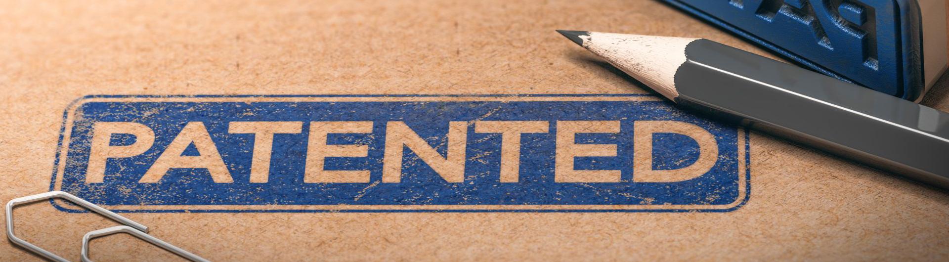The word “Patented” is stamped in blue ink on a brown folder. The ink is surrounded by a paper clip and gray pencil.