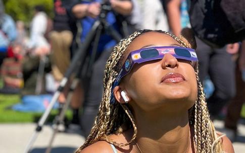 Student gazes up at the sun wearing eclipse glasses