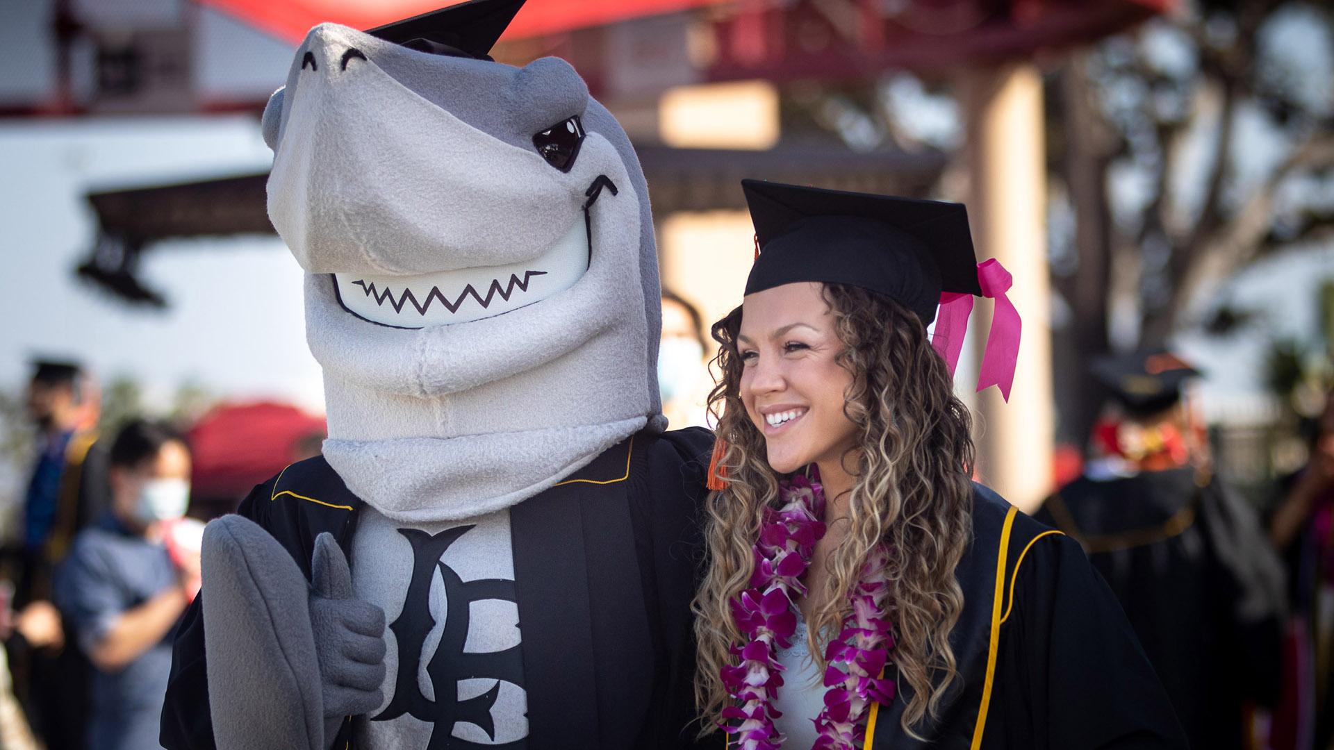 Female graduate student poses with Elbee the shark mascot