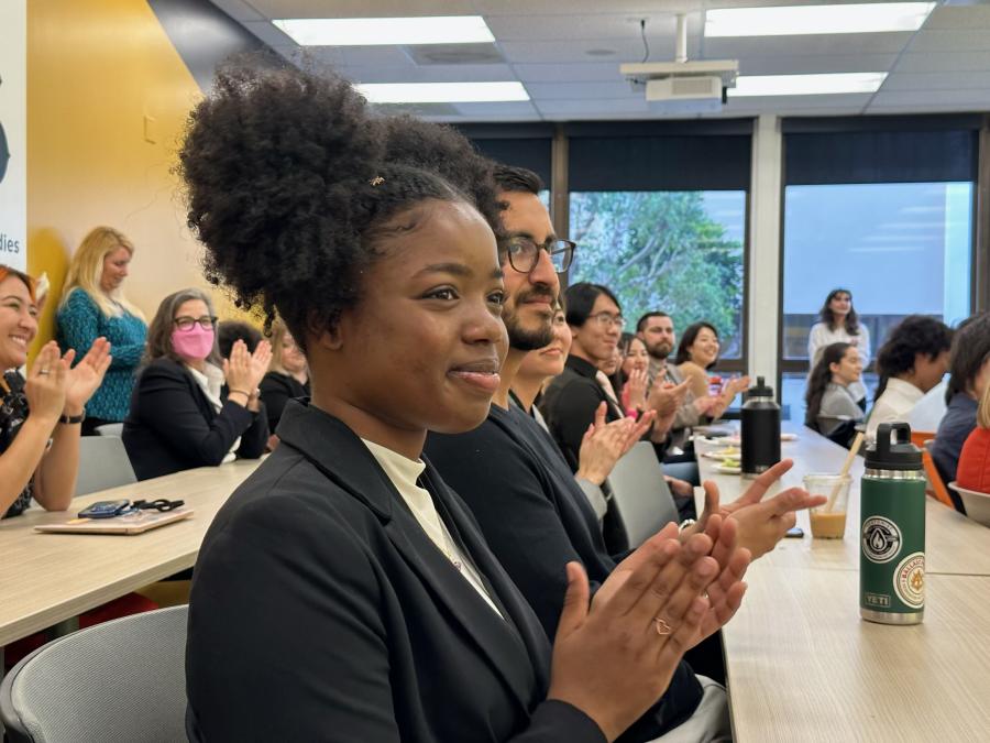 Alyssa Reamer claps while sitting at a table at a CSULB Student Research Competition.