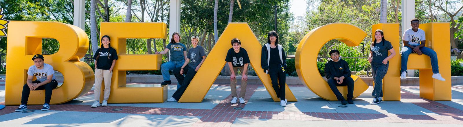 Students hanging out on the Beach sign at CSULB smiling for the camera. 