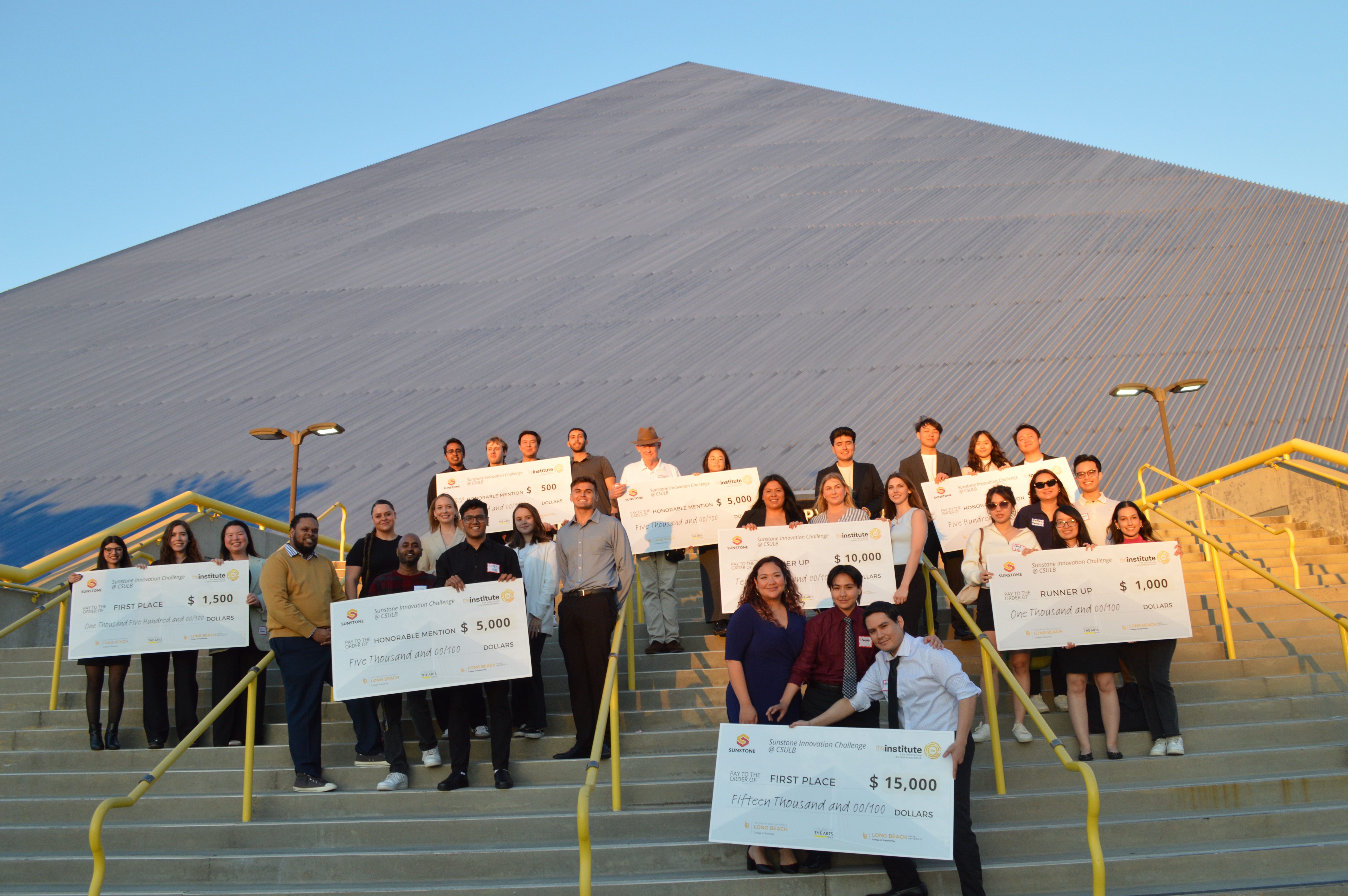 group of people posting in front of pyramid on stairs with jumbo checks
