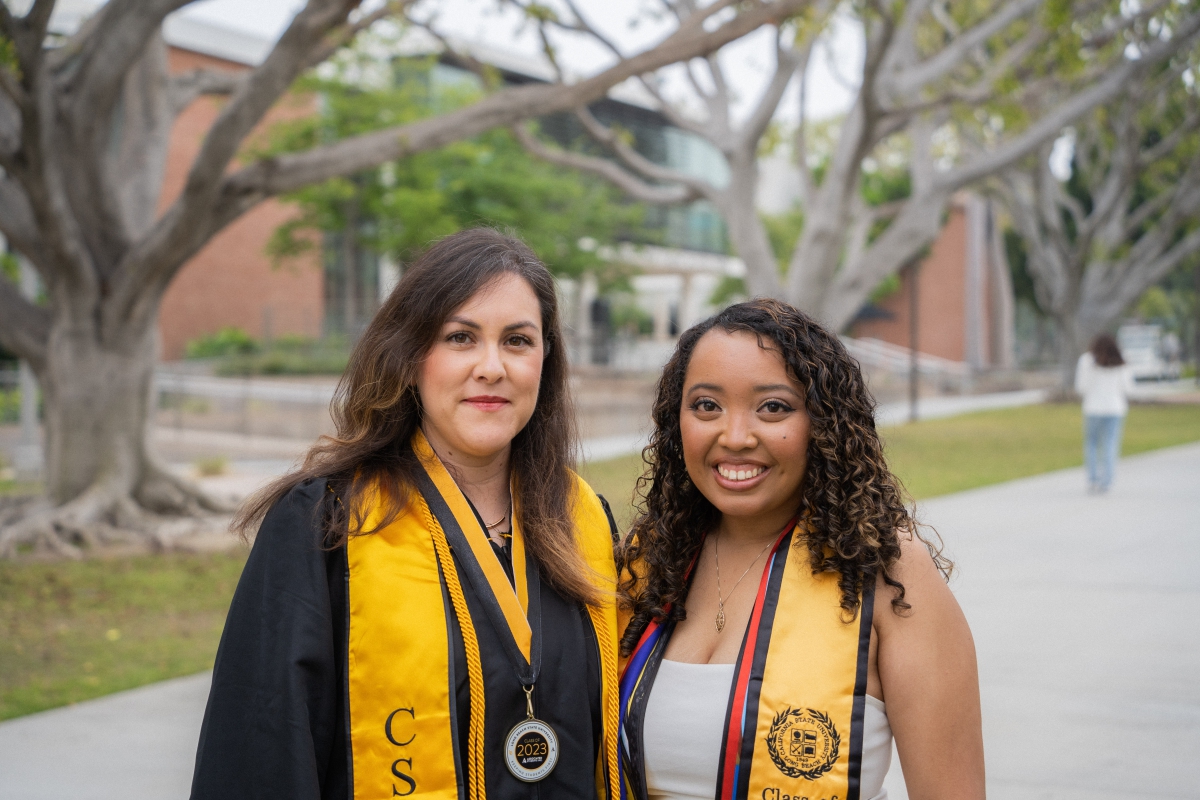 Two graduating students stand smiling side by side.