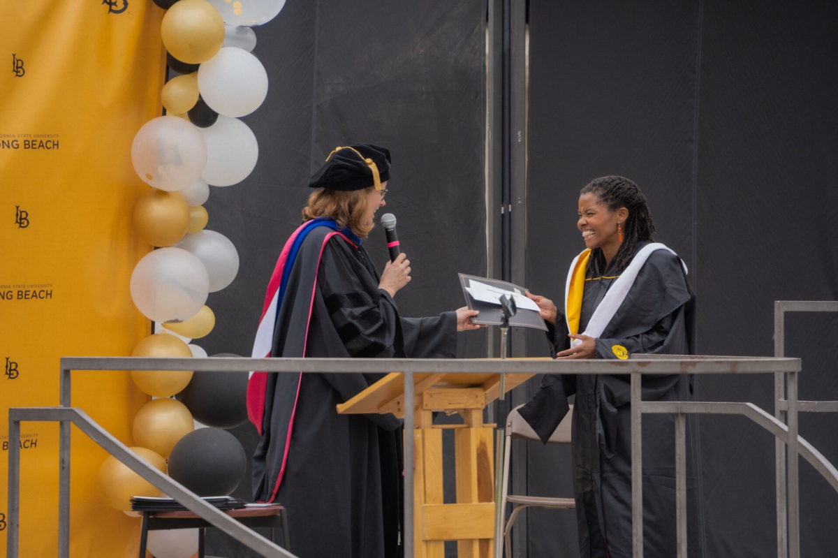 Dr. Hall smiles and hands student paper on the graduation stage.