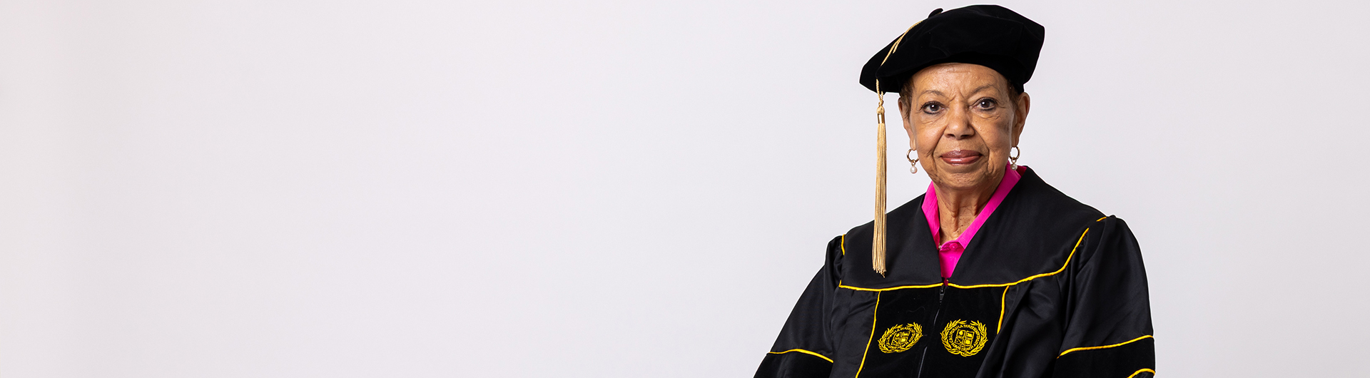 A person wearing academic regalia with embroidered seals sits facing forward