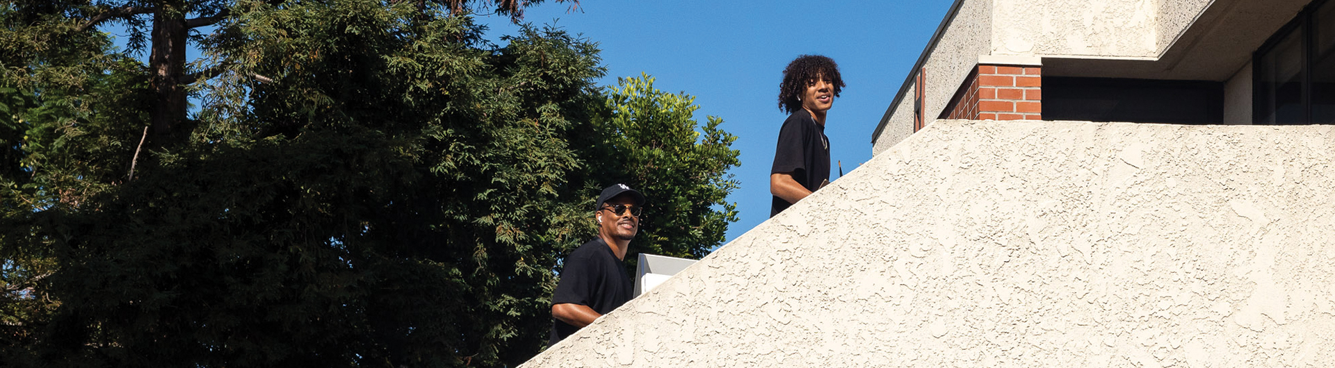Two people walk up an exterior stairwell carrying items.