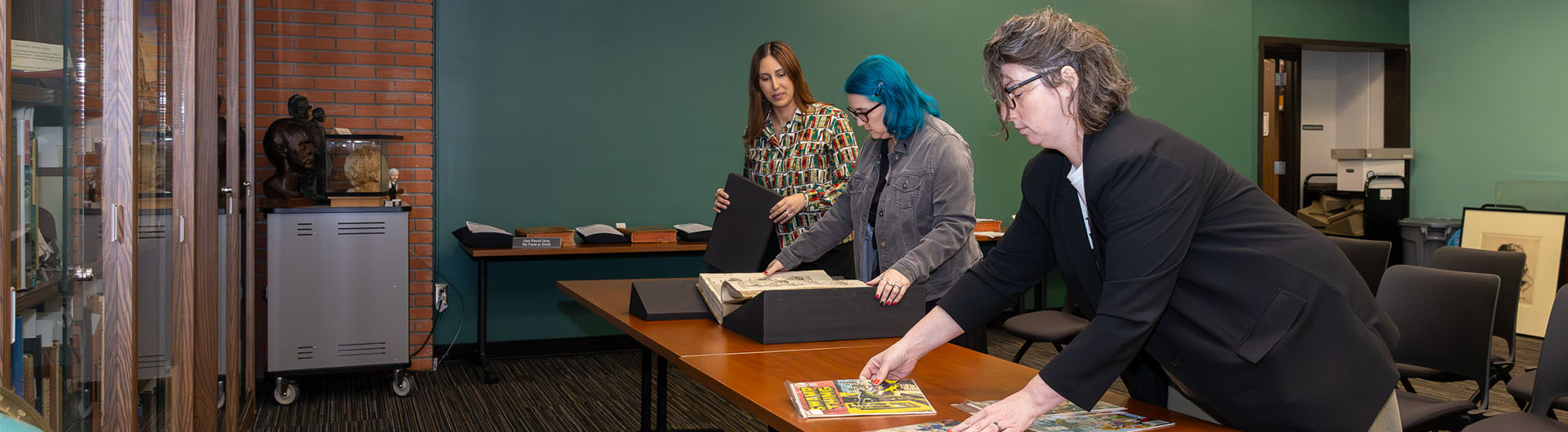 Three people bend over a long table setting up materials