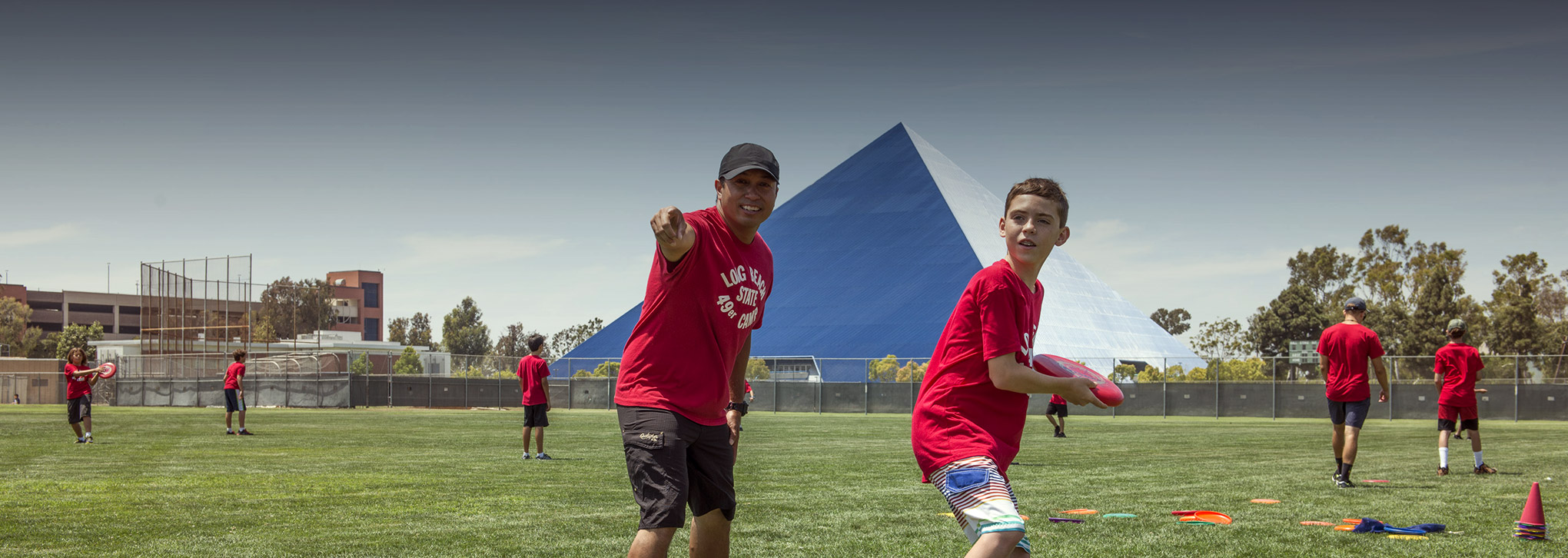Page banner: young students playing ball on campus field, pyramid is seen in the background.