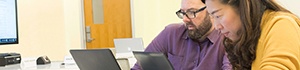 two faculty working on laptops in classroom