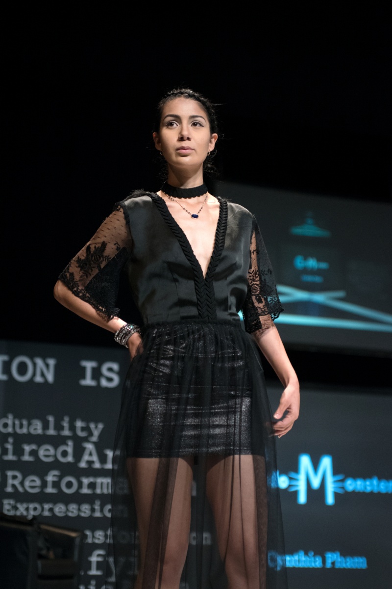 A model walks the runway wearing a black, gauzy dress. 