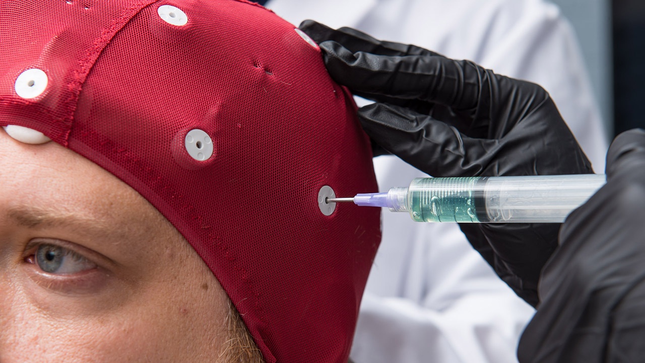 Student injects a lubricant into a skull cap for an EEG screening.