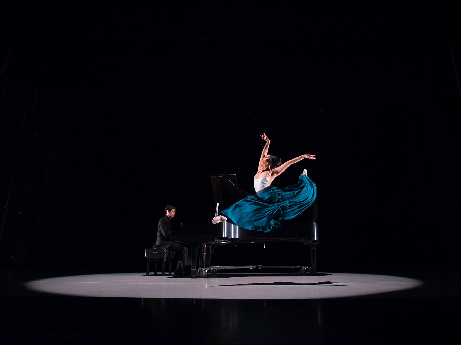 Dancer leaps into air as a Pianist plays music. Photo by Gre
