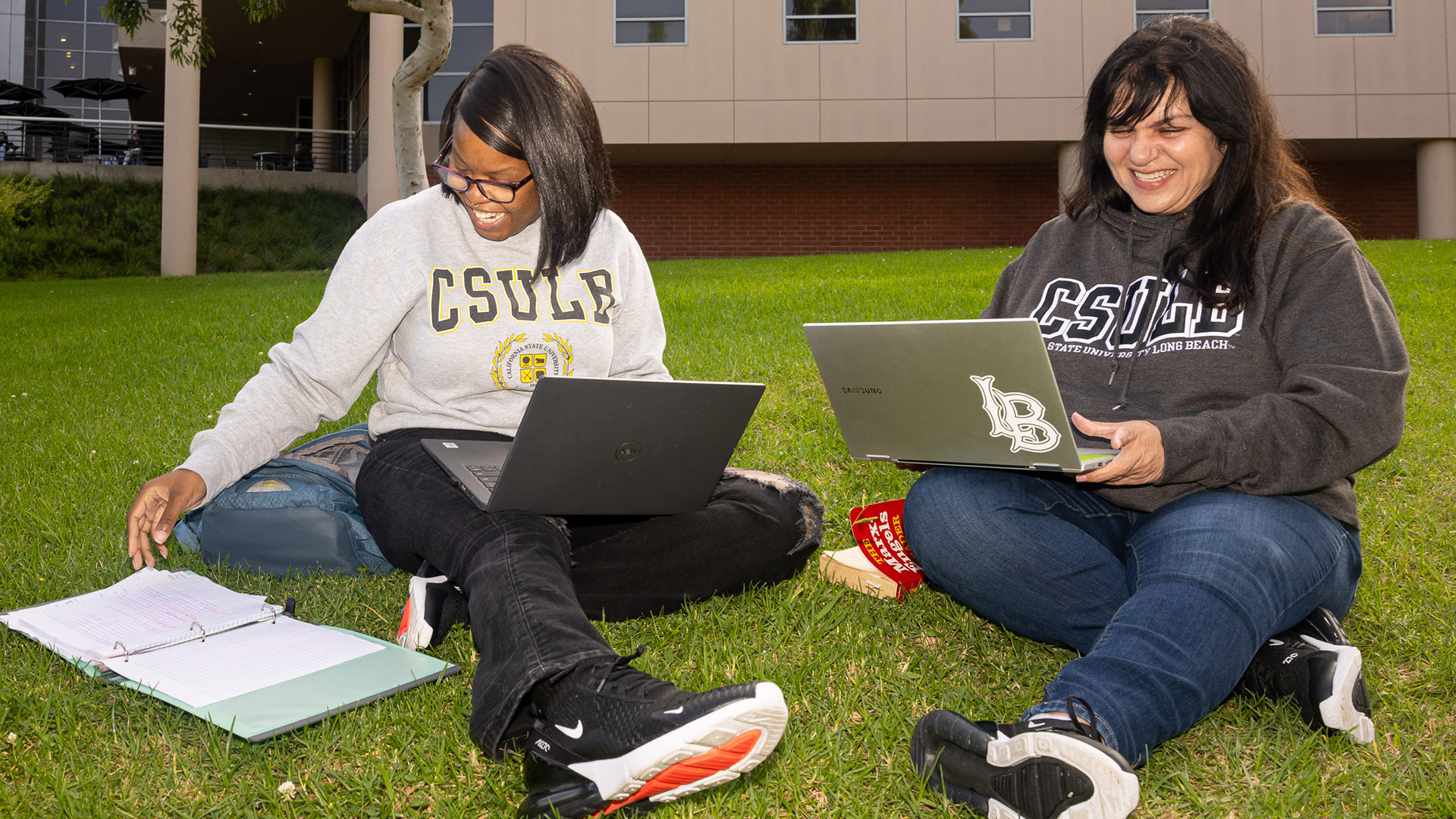 Students sit on grass while working on computers