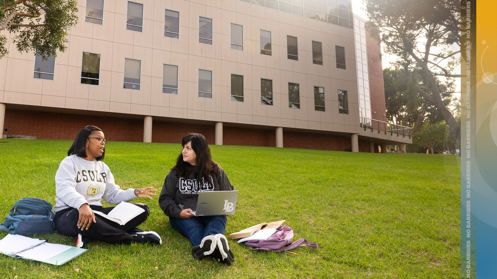 Students sit on grass while working on computers