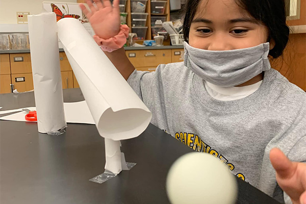 child watching a ball slide out of a paper tube