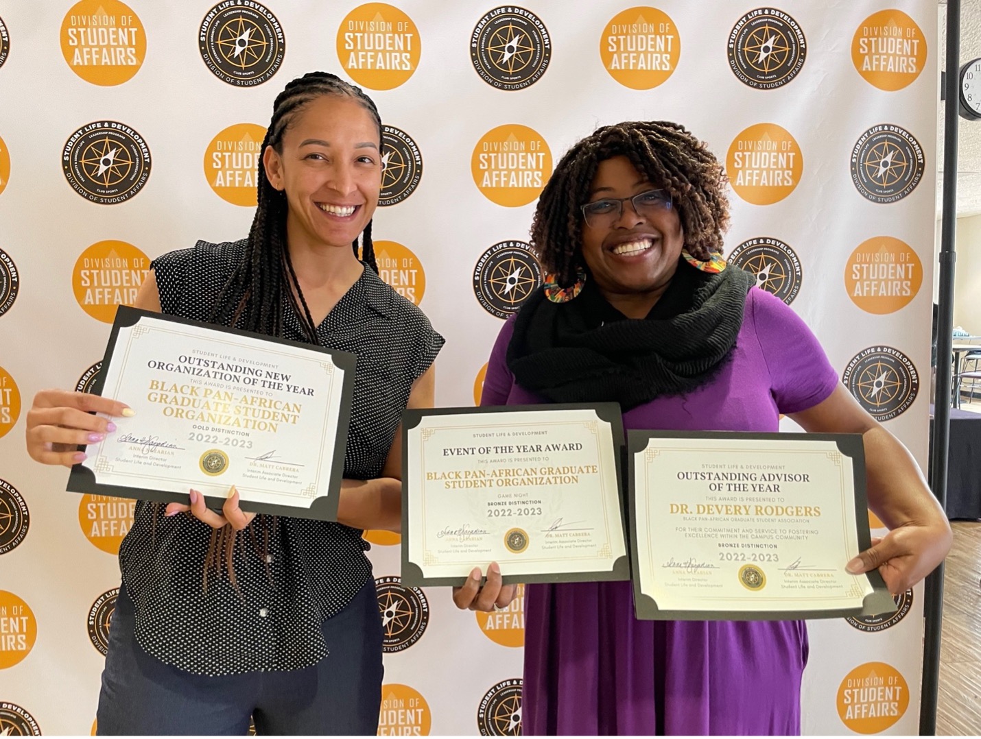 Two women hold up awards they received at an awards ceremony