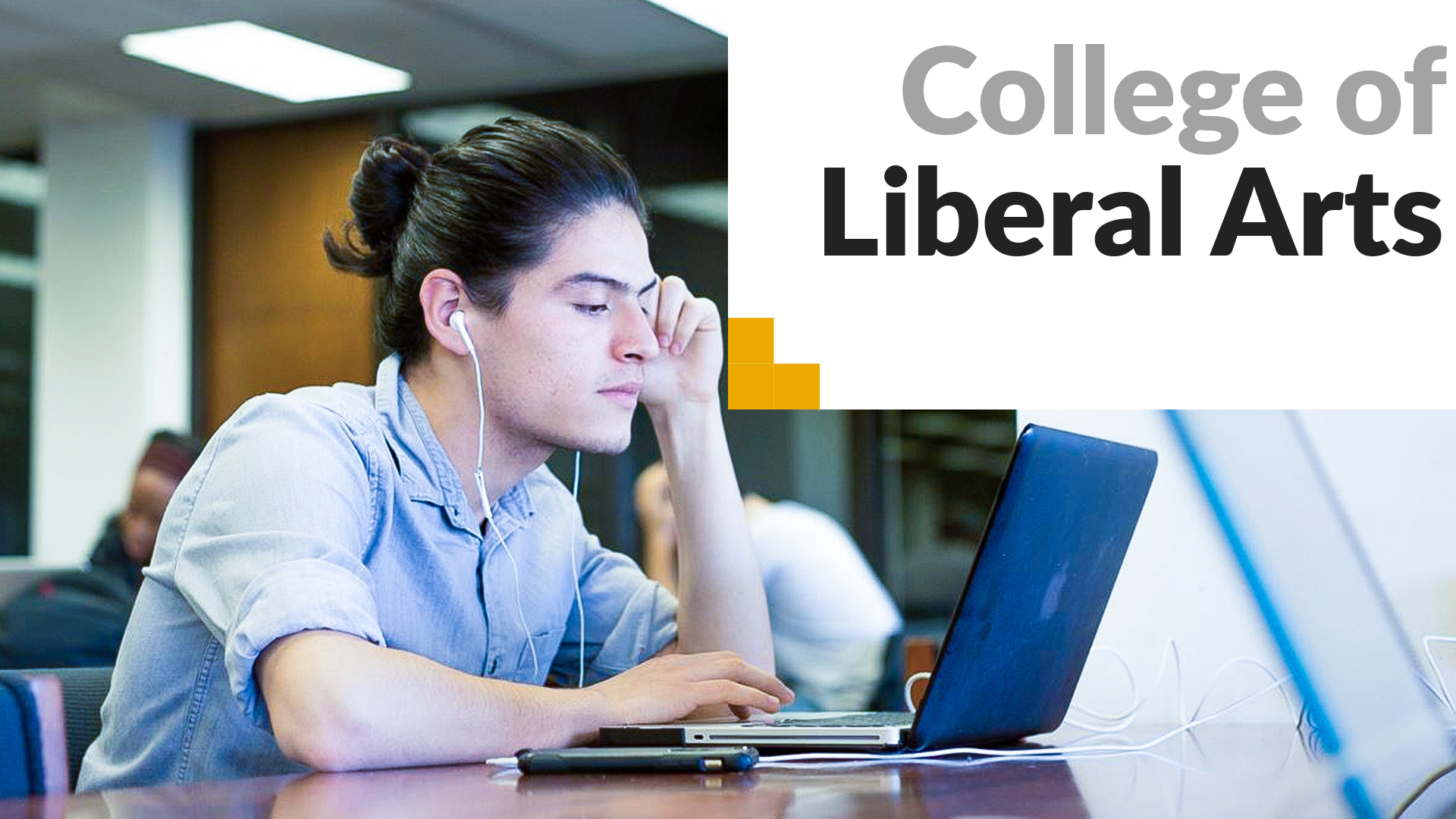 College of Liberal Arts. A student sits in front of his laptop with headphones in. 