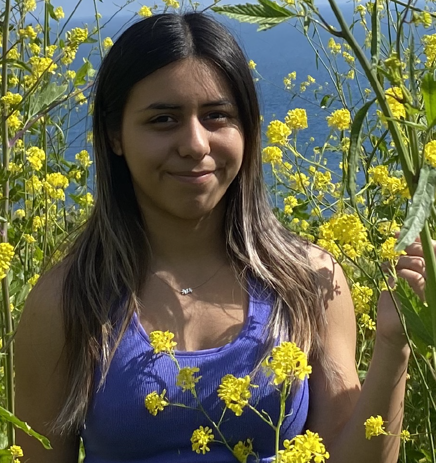 A photo taken of Gizelle Vallejo in a field of tall, yellow flowers.