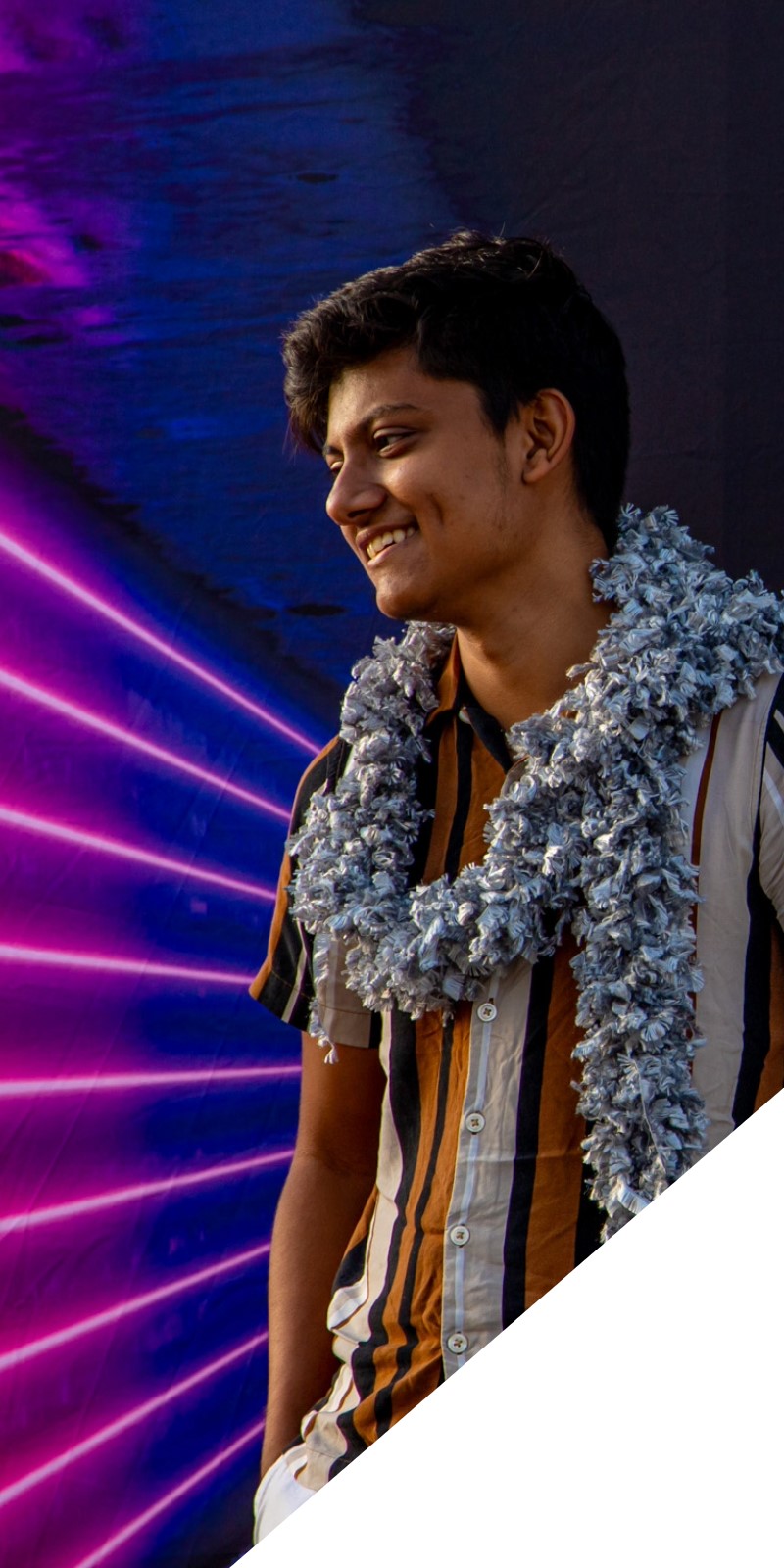 A student smiles while bright blue and pink lights illuminate behind him. 