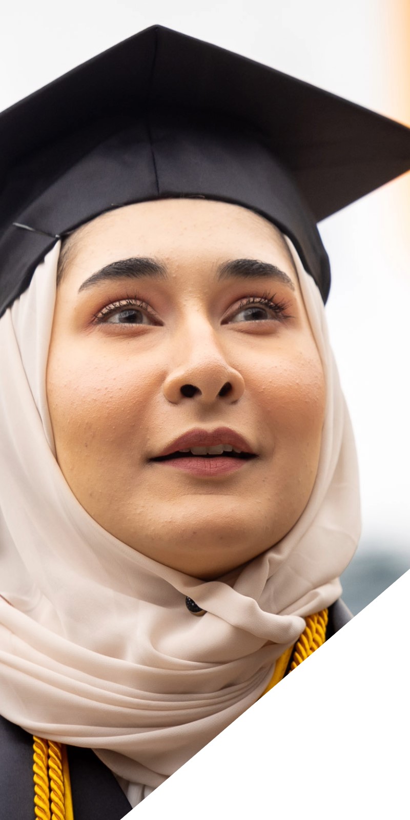 A student looks off camera in a cap and gown at graduation. 