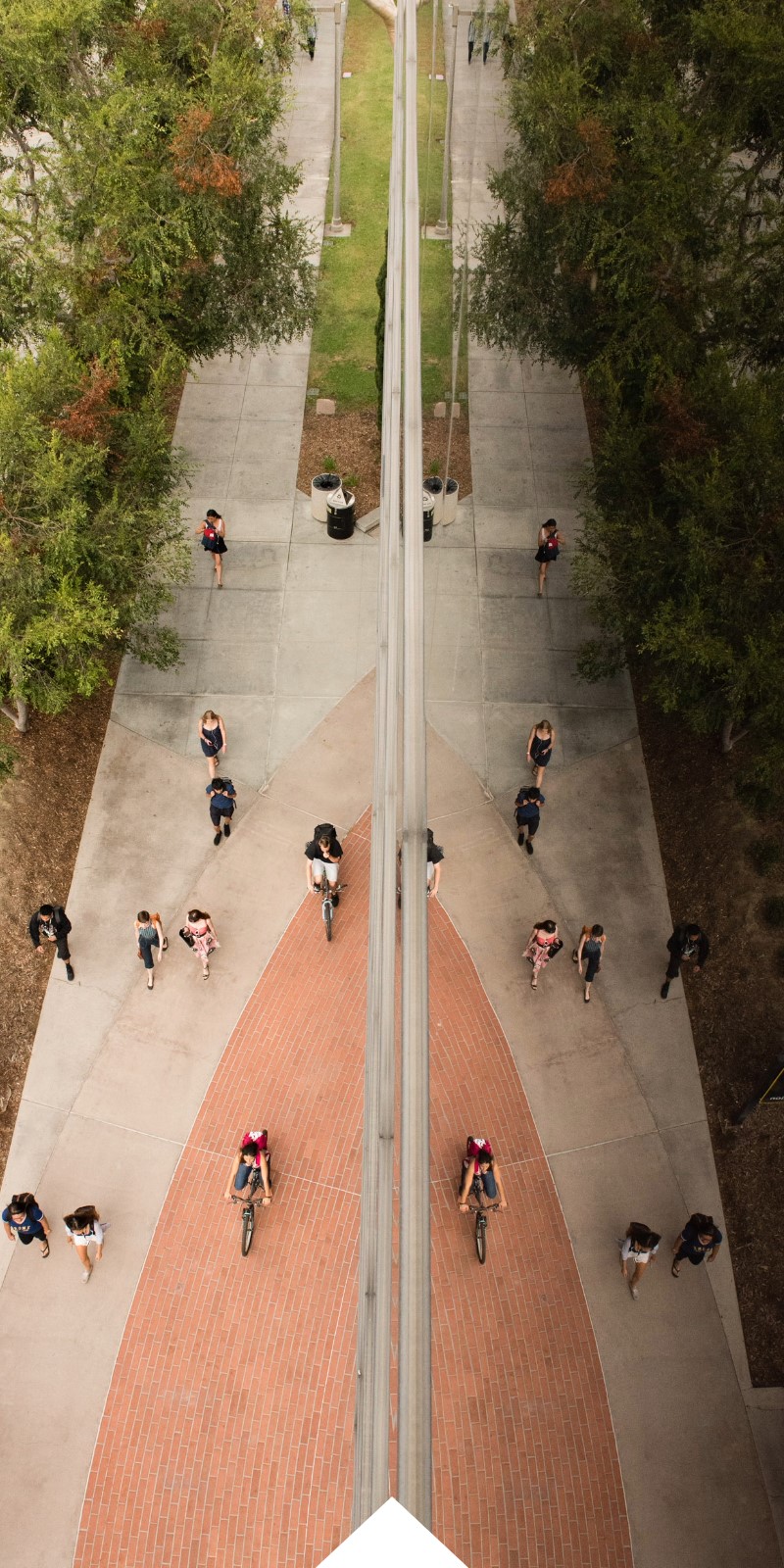 Students walk and bike past the College of Business building. Their reflection is mirrored in the glass siding of the building. 