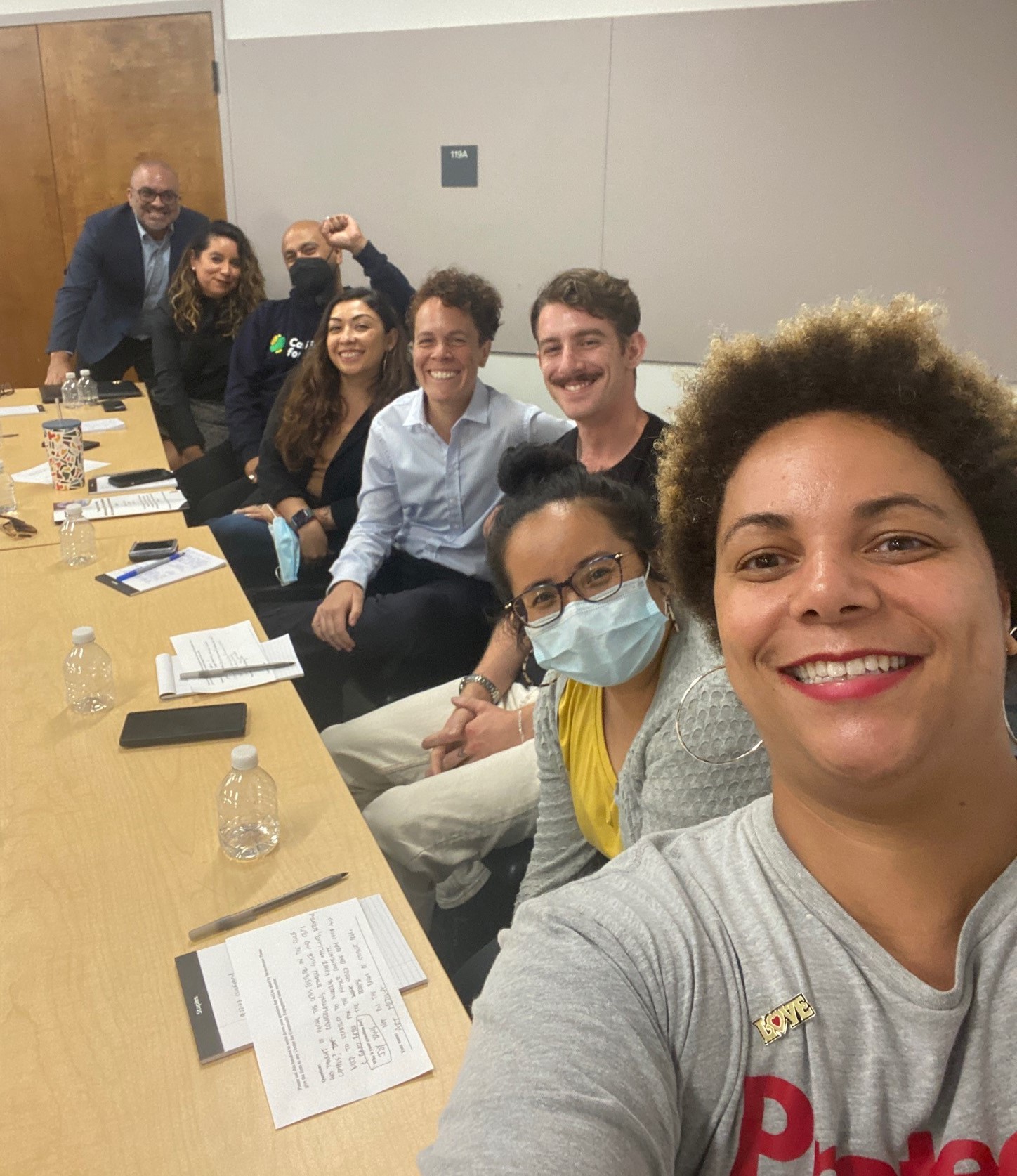 8 community members are seated at a table taking a selfie