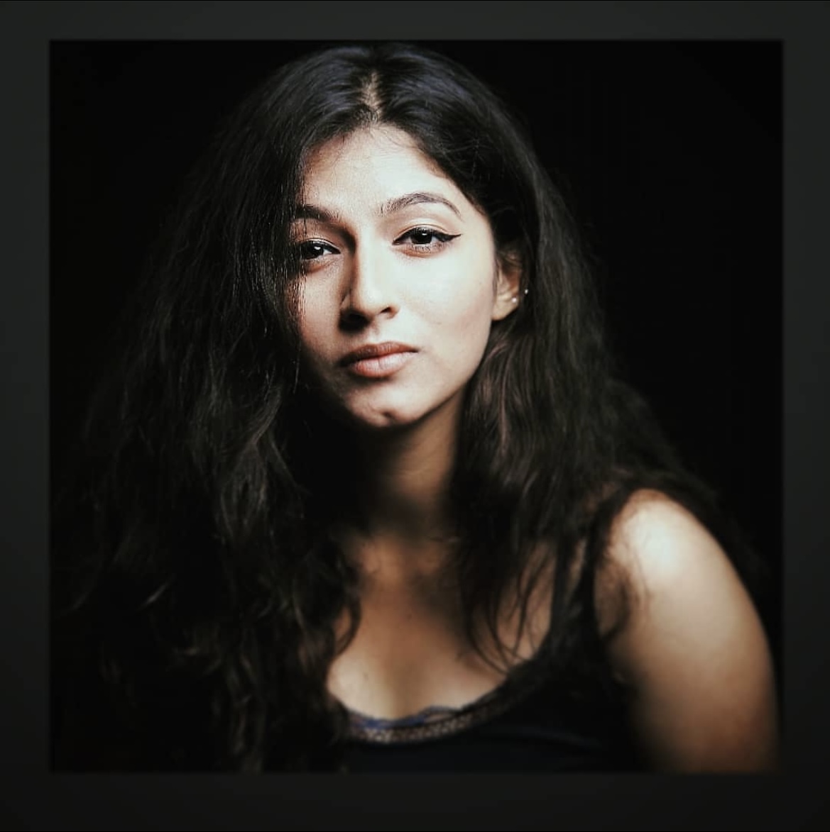 Bhargavi Sardesai Headshot. Her hair is down, she is in a black tank top against a black background.