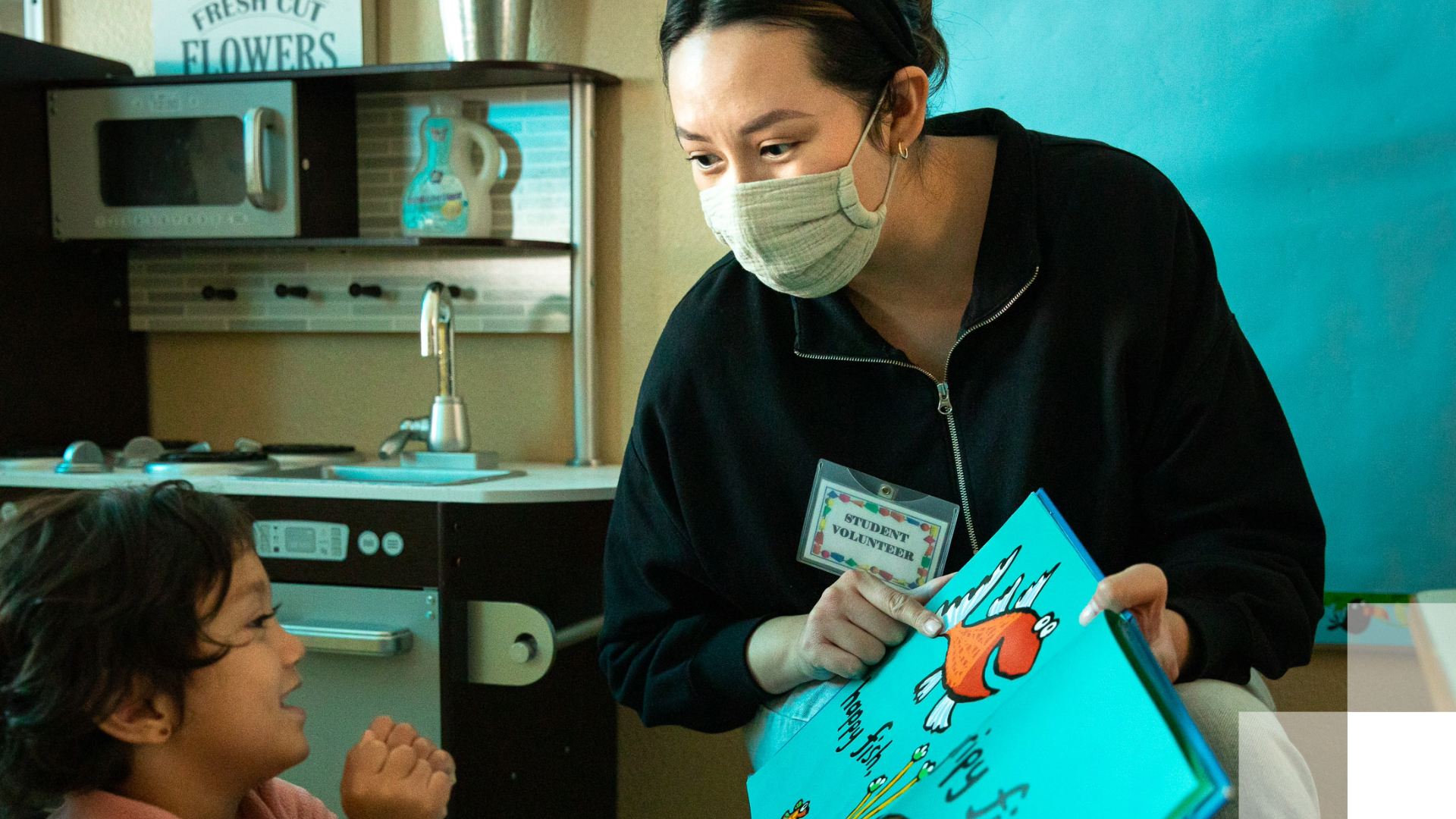Ballmer Scholar - Beach 2030 Teacher reads a book with a fish on it to small child.