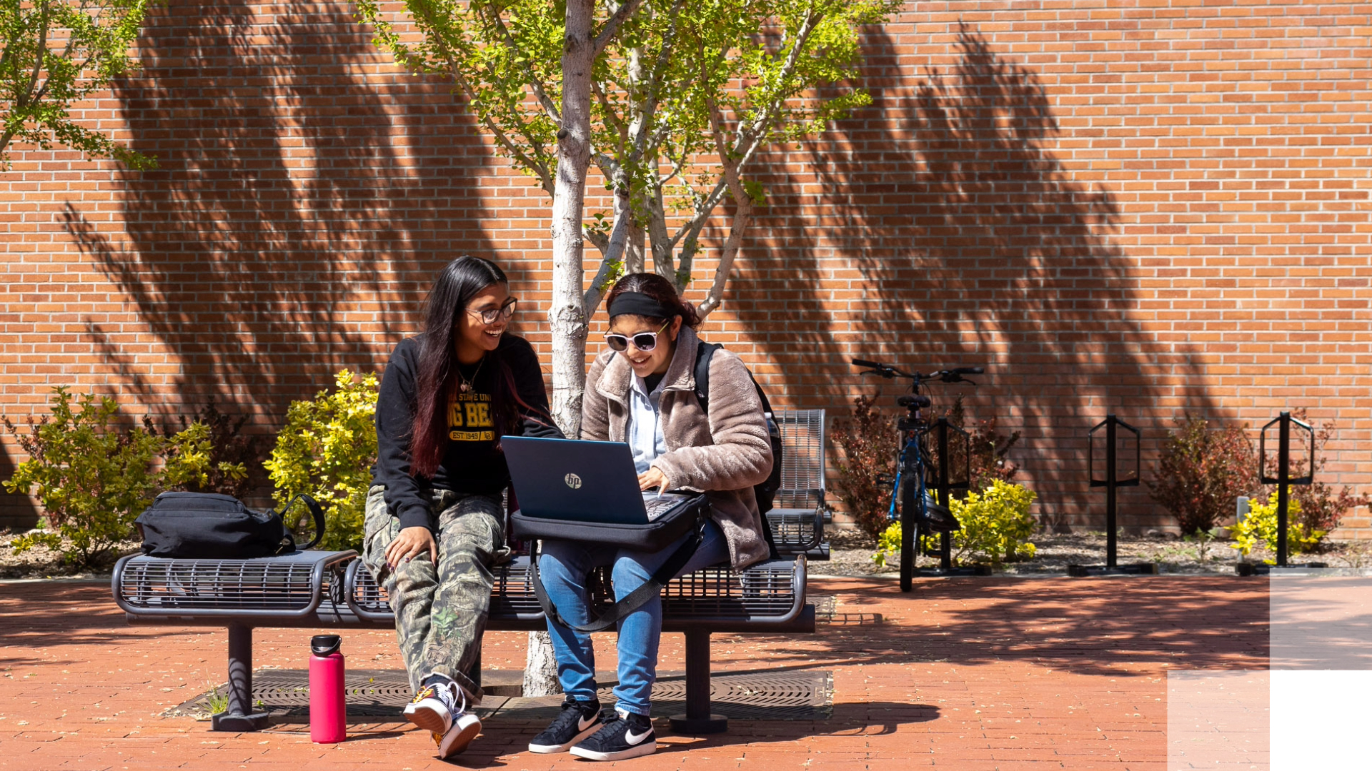 Day 1 Textbook Access - B2030 Two students sit on a bench outside and look at a laptop.
