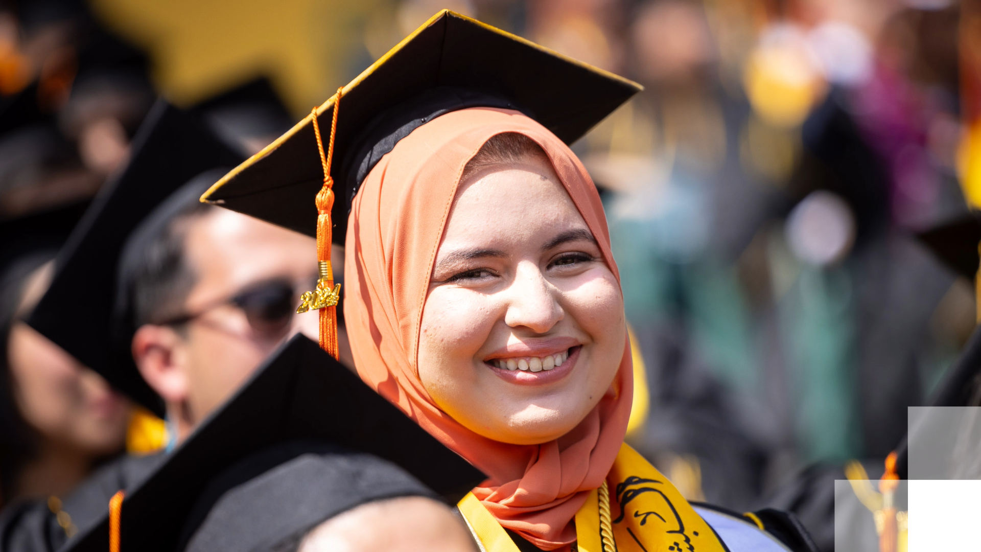 A student in a cap and gown smiles at graduation.