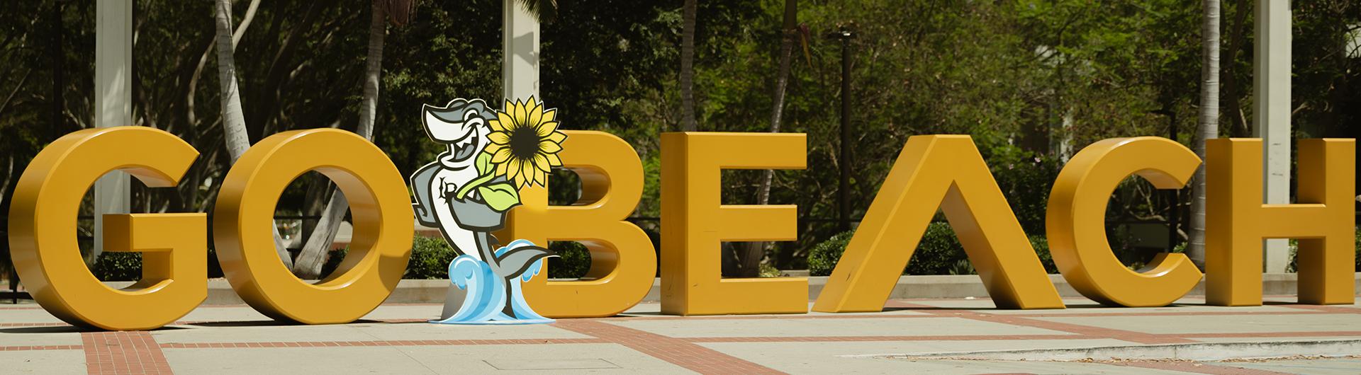 Elbee with a sunflower in front of Go Beach sign