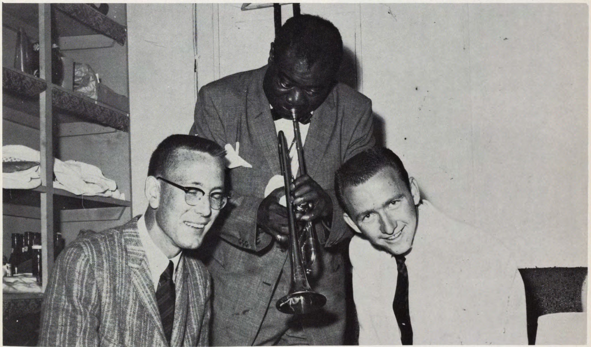 Louis Armstrong on campus A trumpet player stands between two smiling men in a small room.