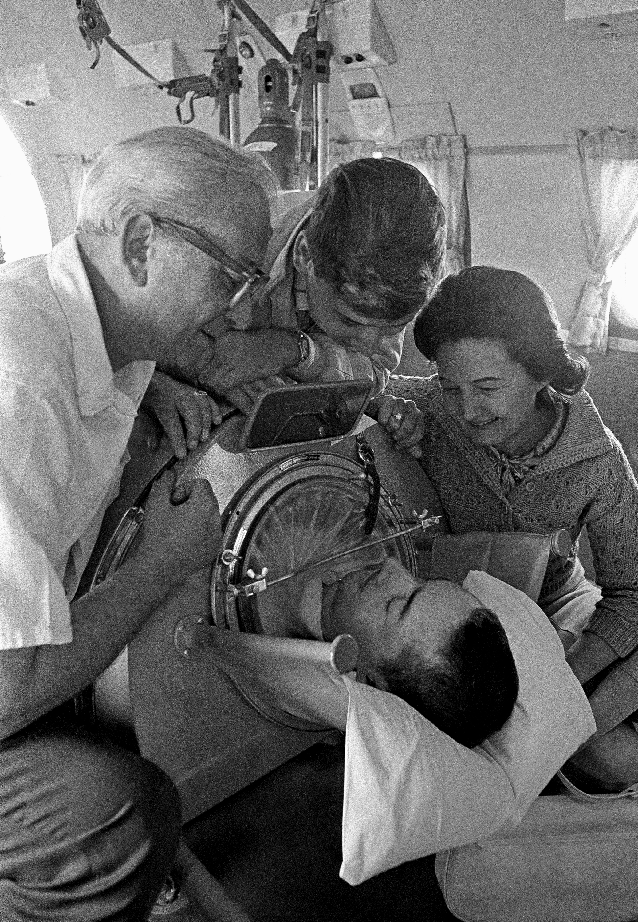 Bob Rubin says goodby to his family on an Air Force jet. (This was licensed picture, do not reuse) Three people smile and look at a person inside an iron lung, engaged in conversation.