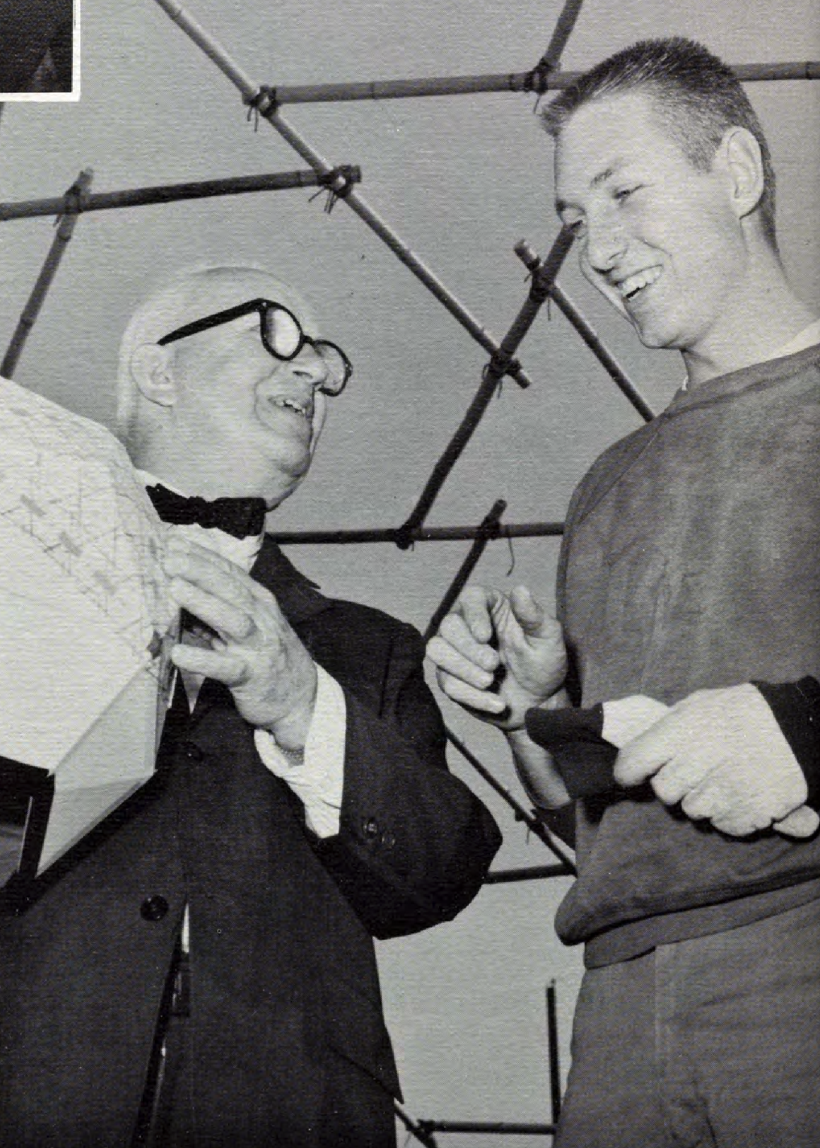 Buckminster Fuller and a student Two people, one holding a geometric object, smile while talking under a structure of connected rods.