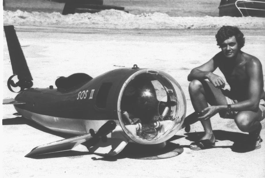 Don Nelson and his submersible camera A person crouches next to a small personal submersible on the beach.