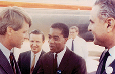 Joseph White stands Robert F. Kennedy outside an aircraft. Joseph White stands with other men in suits, including Robert F. Kennedy, converse outside an aircraft.