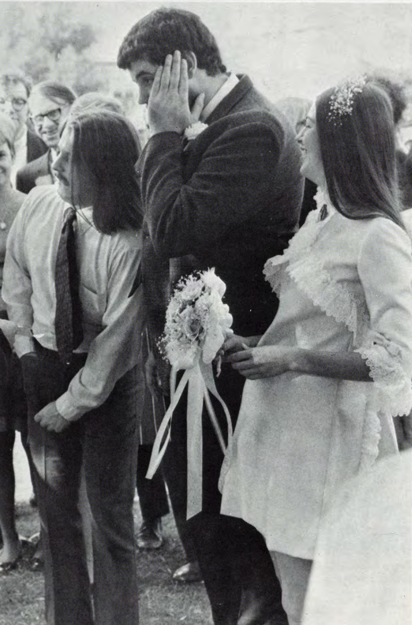 Carolyn Roller and Craig Hendricks ‘70 get married on campus A newlywed couple and a guest stand together, the groom appearing distressed as another man rummages through his pocket.