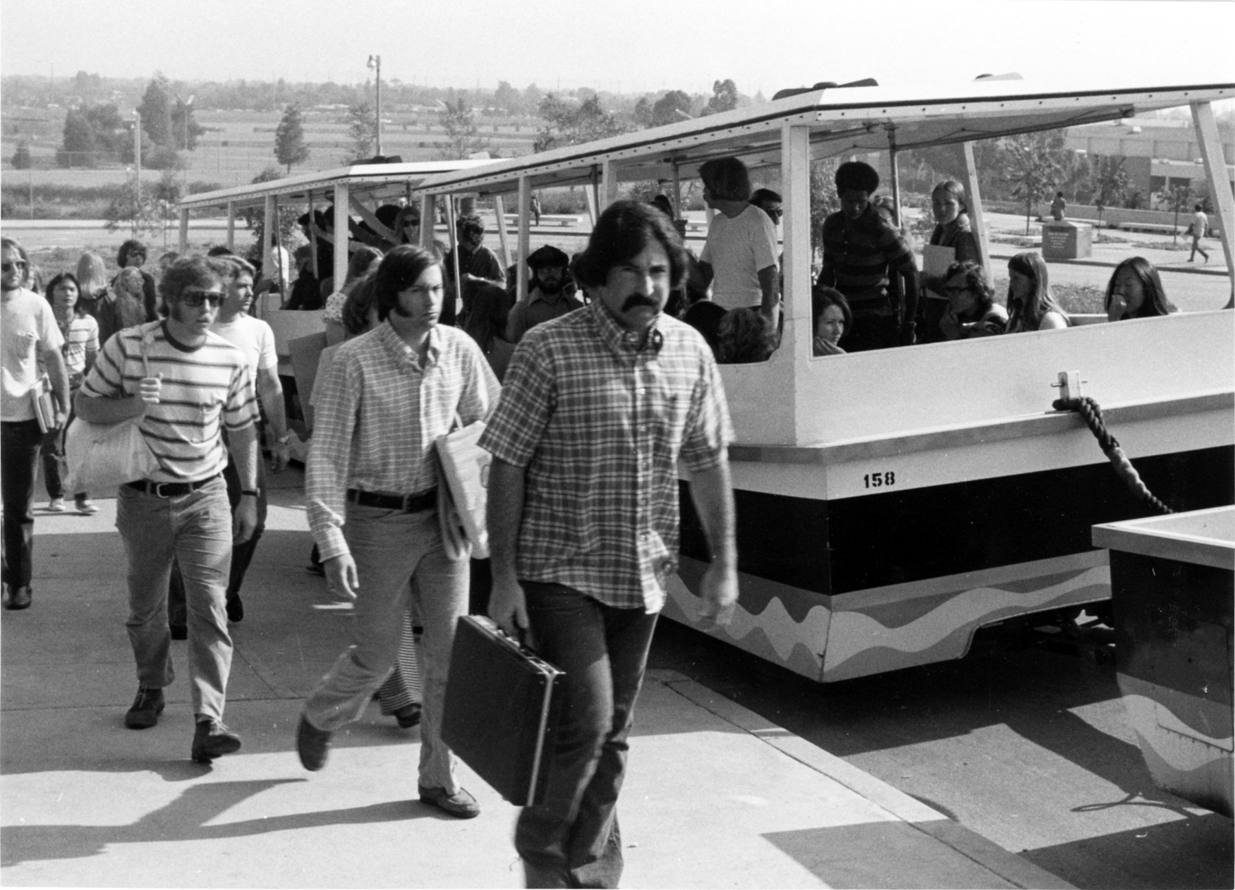 CSULB sudents exit a campus tram Students exit a campus tram while others board, carrying books and bags.