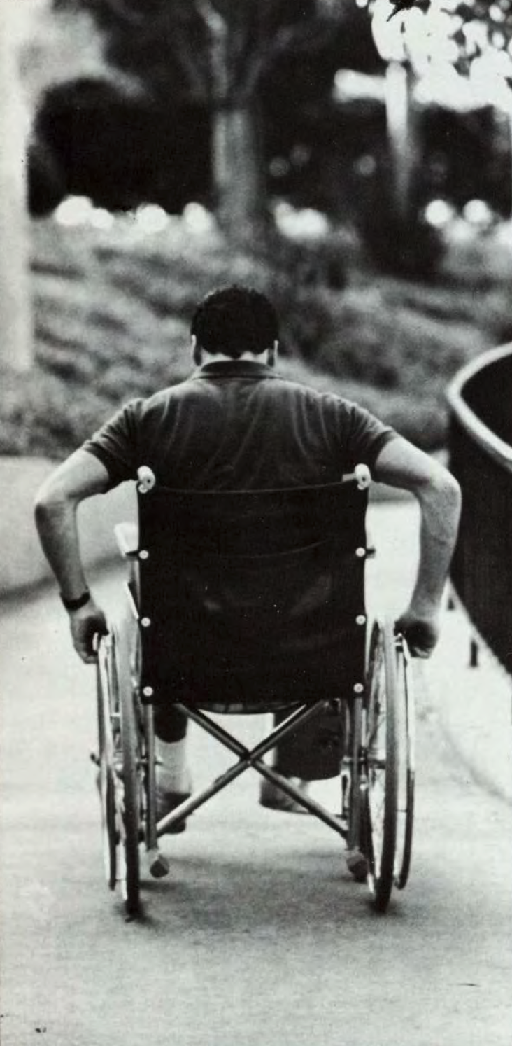 A person pushes a wheelchair along a curved path on campus A person pushes a wheelchair along a curved path.