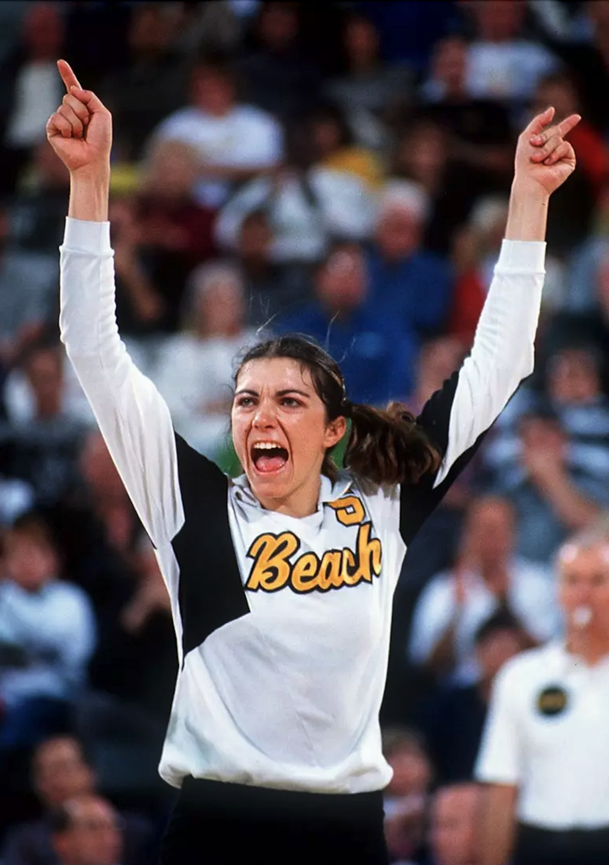 Misty May Volleyball player enthusiastically raises both arms, celebrating.
