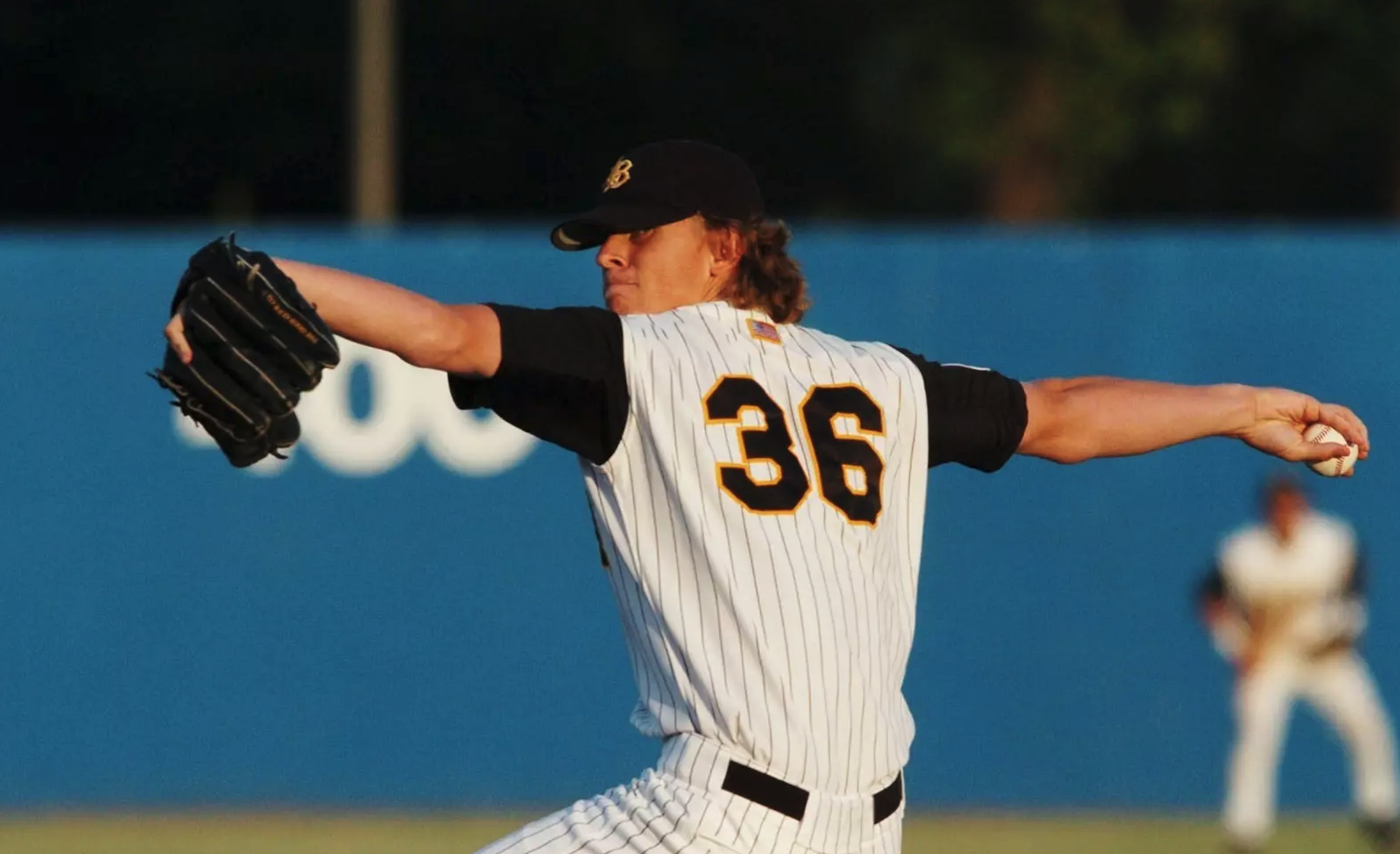 Dirtbag Jered Weaver in his "36" uniform Jered Weaver in a white pinstripe uniform and black cap winds up to throw, with a fielder visible in the background against a blue wall.