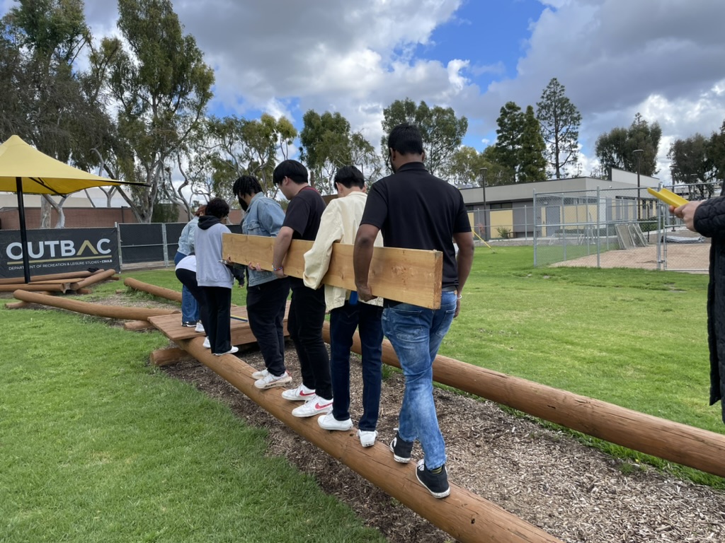 students working together to carry a wooden plank