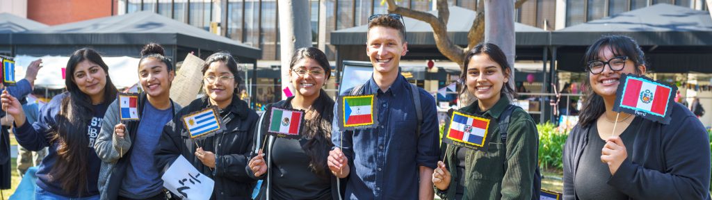 International Mother Language Day A group of students stand in a row facing forward, each holding a flag of a multicultrual background.