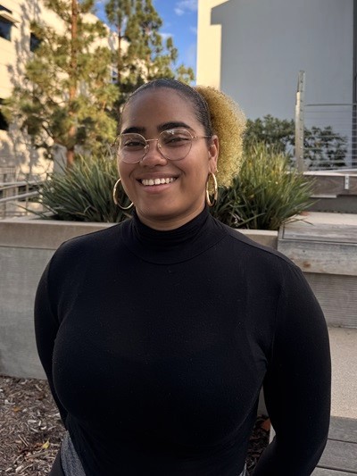Anthonia Wright Anthonia Wright standing in front of a concrete planter with plants behind her