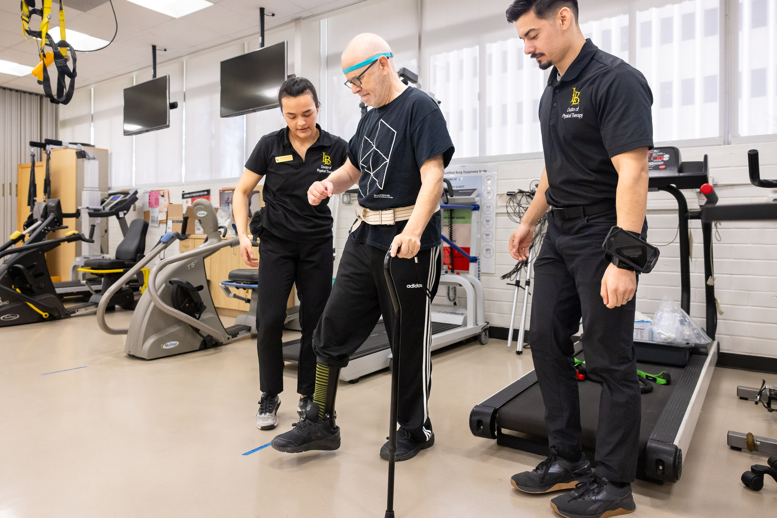 Two students helps a Neuro Lab client as he uses a cane to walk